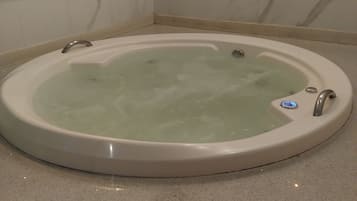 A round bathtub with a control panel, set on a speckled floor, against a wall with a marble pattern.