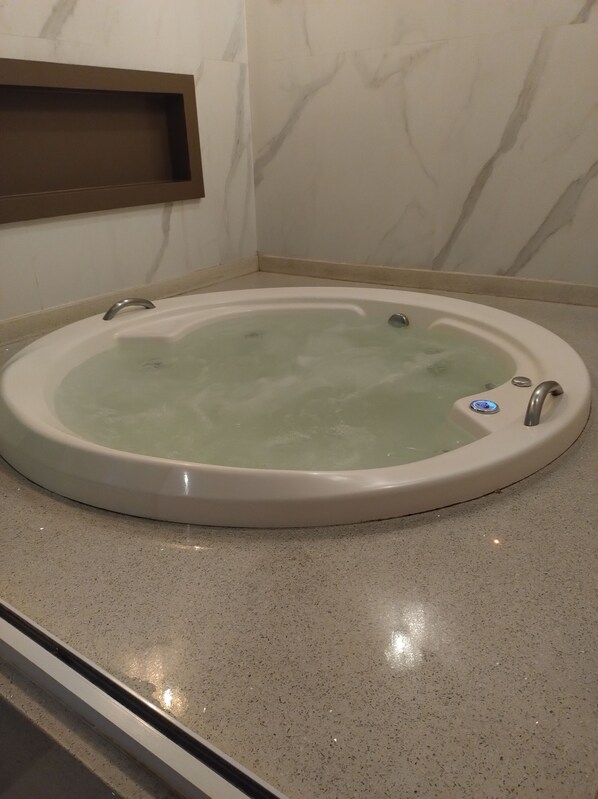 A round bathtub with a control panel, set on a speckled floor, against a wall with a marble pattern.