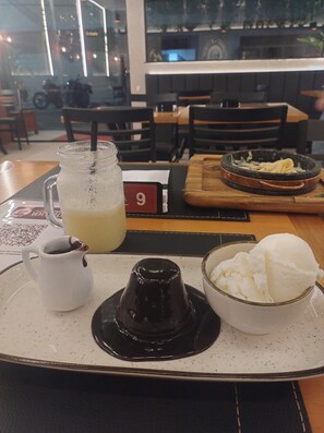 A table with a tray containing a glass of iced tea, a small pitcher of coffee, and a bowl of ice cream.