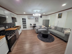 A modern kitchen with a stove, oven, and cabinets, a dining area with a table and chairs, and a living room with a sofa and a coffee table.