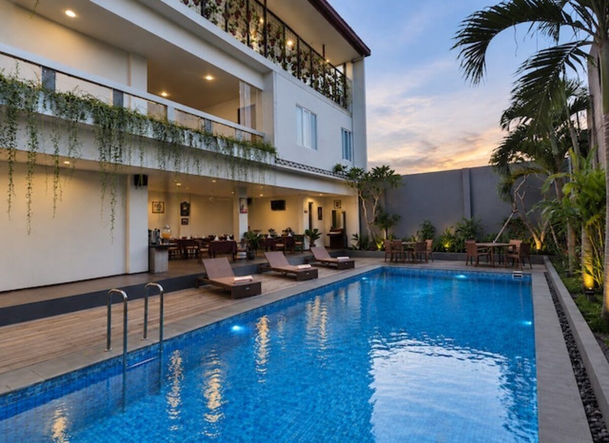 Un hotel con piscina, mobiliario exterior y balcón con plantas.