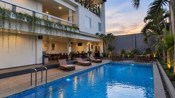 Un hotel con piscina, mobiliario exterior y balcón con plantas.