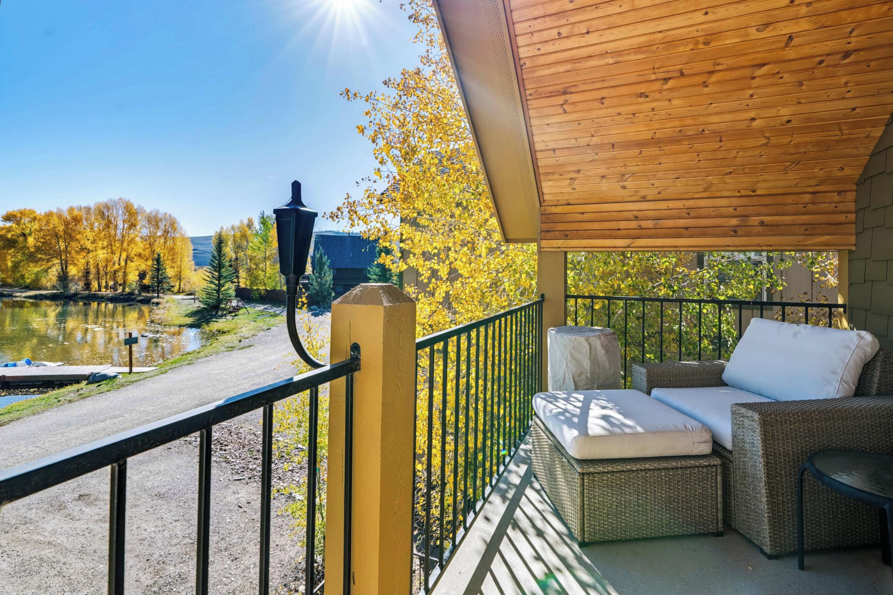 A covered outdoor seating area with a view of a lake and autumn trees.