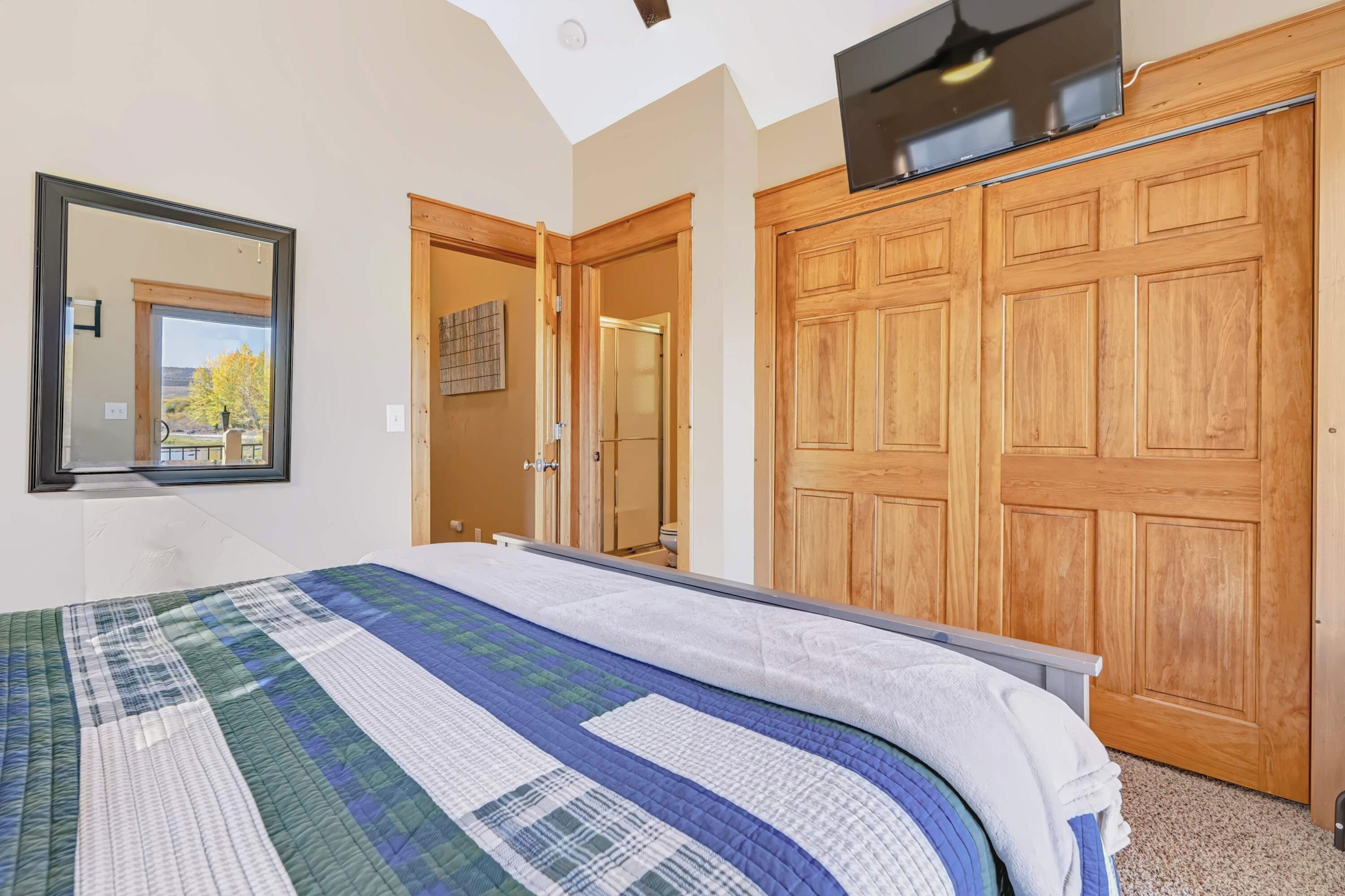 A bedroom with a large bed, a wooden wardrobe, a mirror, and a television.