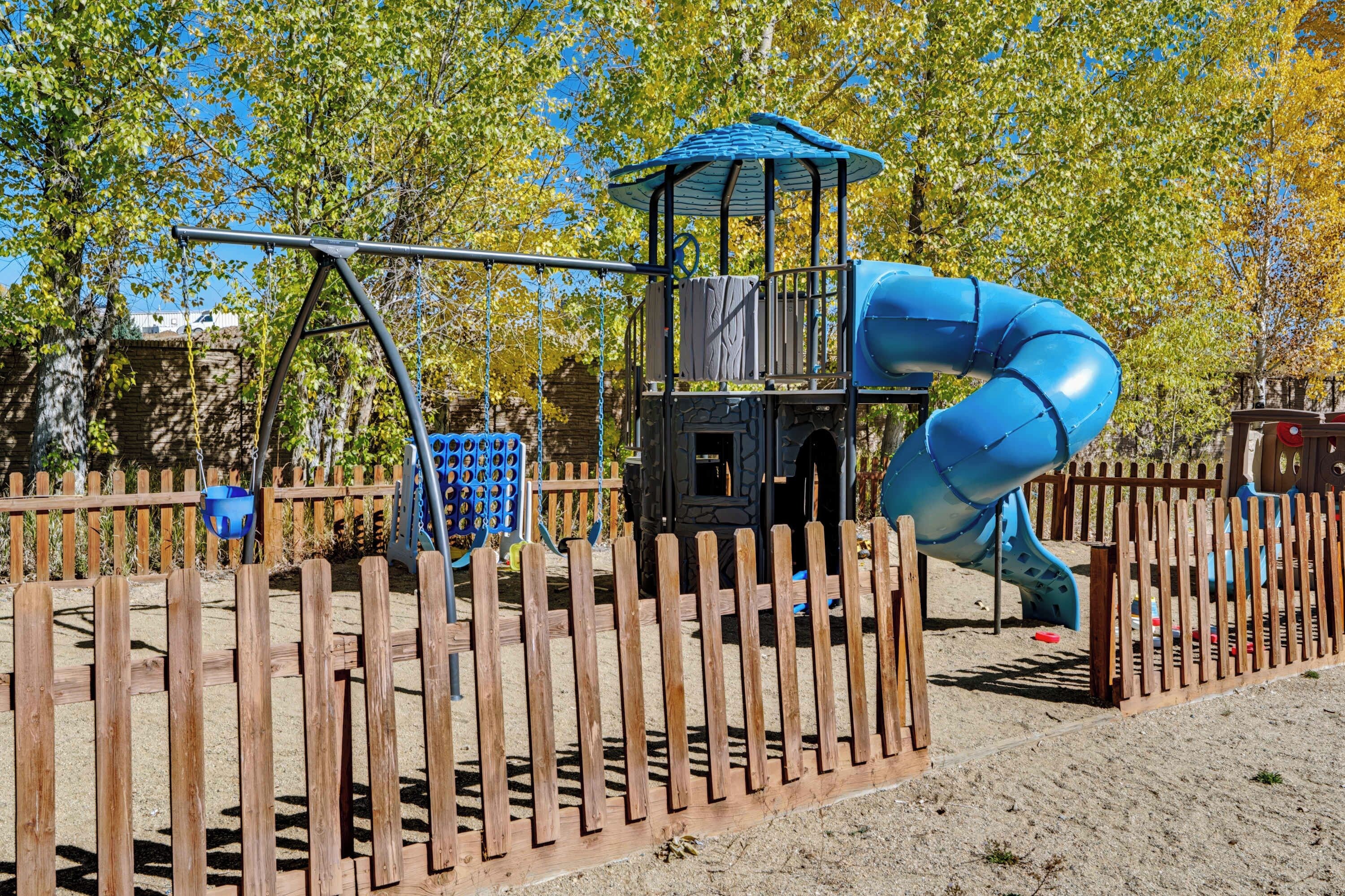 Un parque infantil con tobogán, columpios y una estructura para escalar.