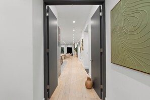 A hallway with a wooden floor, a large vase, and a textured wall art piece. - Fuller Celestia By Alora Reserve (Los Angeles)