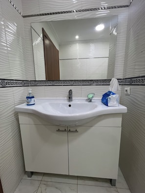 A bathroom with a white sink, a mirror, and a towel dispenser. - New Listing (Tanger)