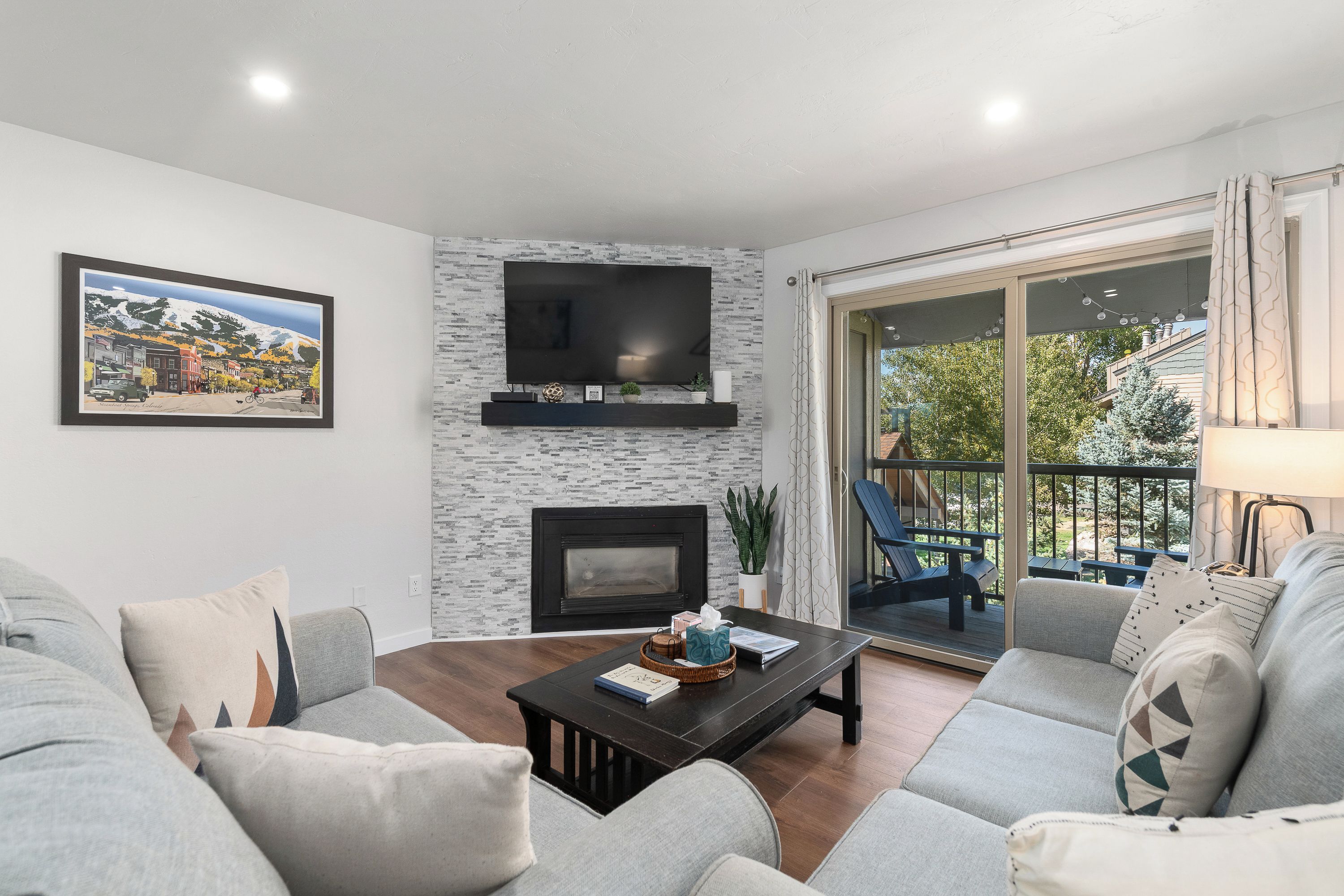 A modern living room with a fireplace, a flat-screen TV, and a balcony with outdoor furniture.
