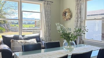 Uma sala de jantar com mesa de vidro, cadeiras pretas, um vaso com flores e vista para o exterior.