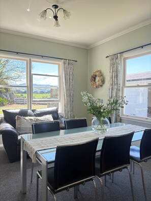 A dining area with a glass table, black chairs, a vase with flowers, and a view of the outdoors. - Clareville Farmhouse - Relax in Peaceful Rural Surroundings Near the Showgrounds (Clareville)