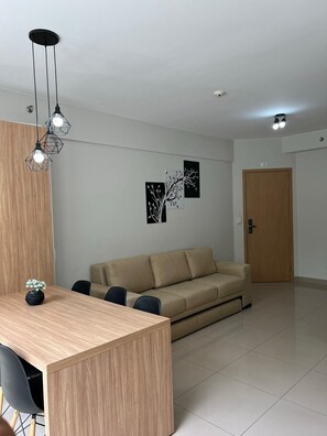 Ein modernes Wohnzimmer mit einem Holzesstisch, einem beigefarbenen Sofa und einer Wandleuchte.