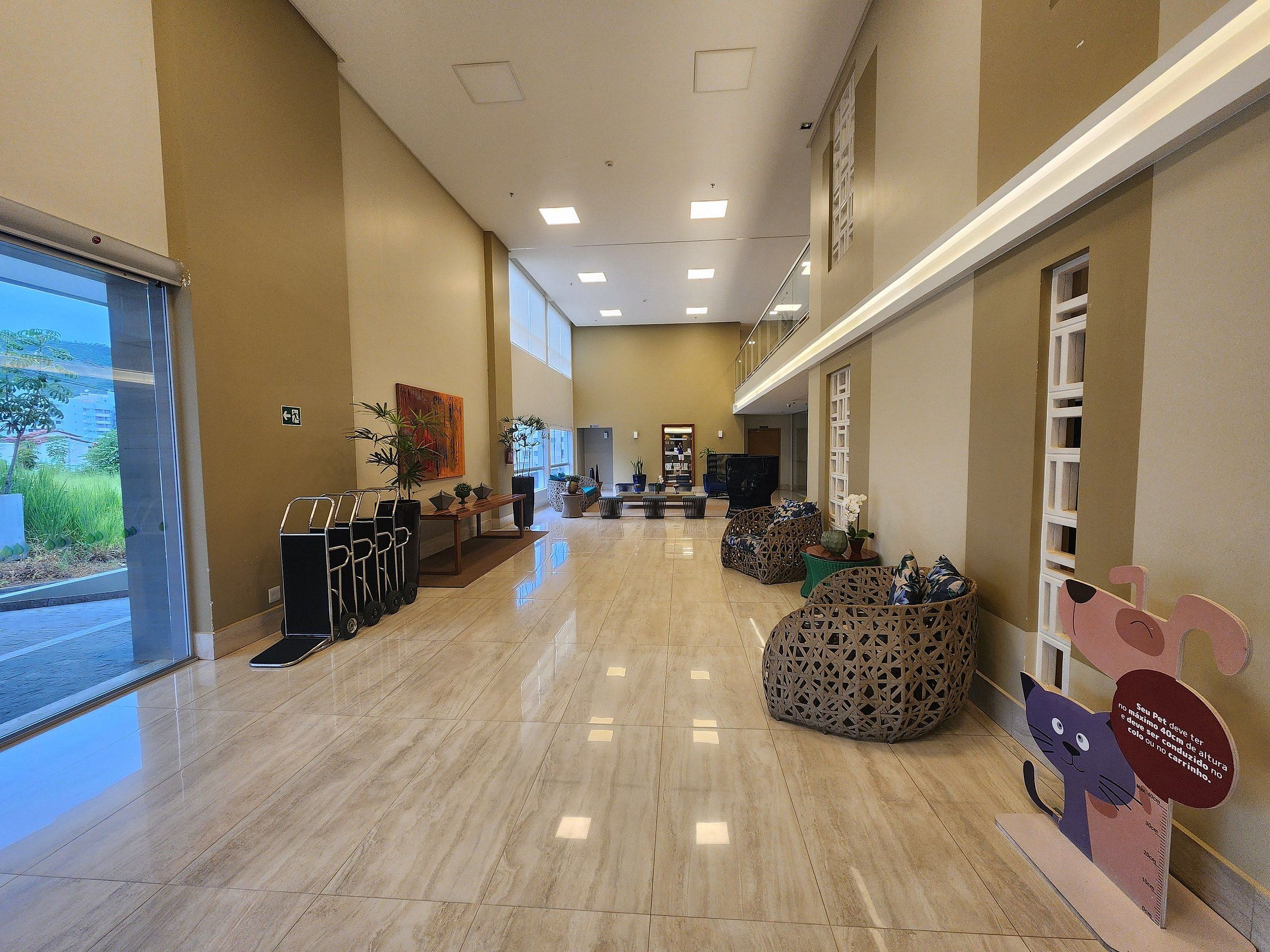 Um hall amplo com piso lustroso, áreas de estar e um balcão de recepção.