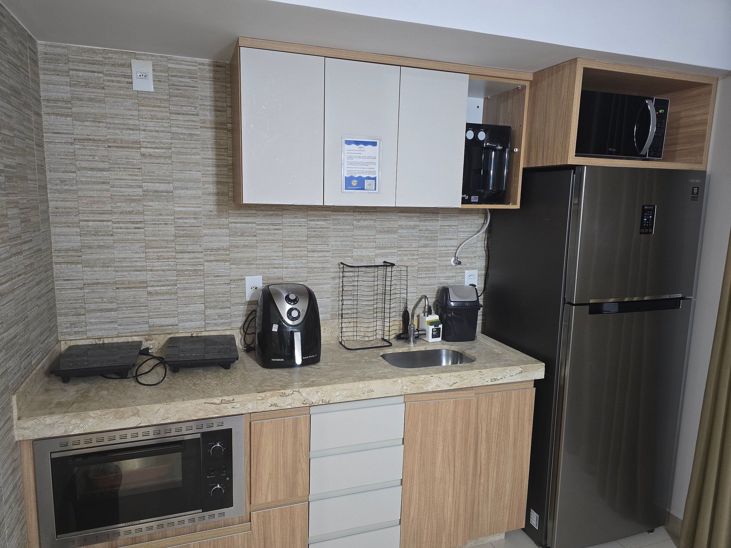 Cozinha moderna com micro-ondas embutido, geladeira de aço inoxidável e cafeteira na bancada.