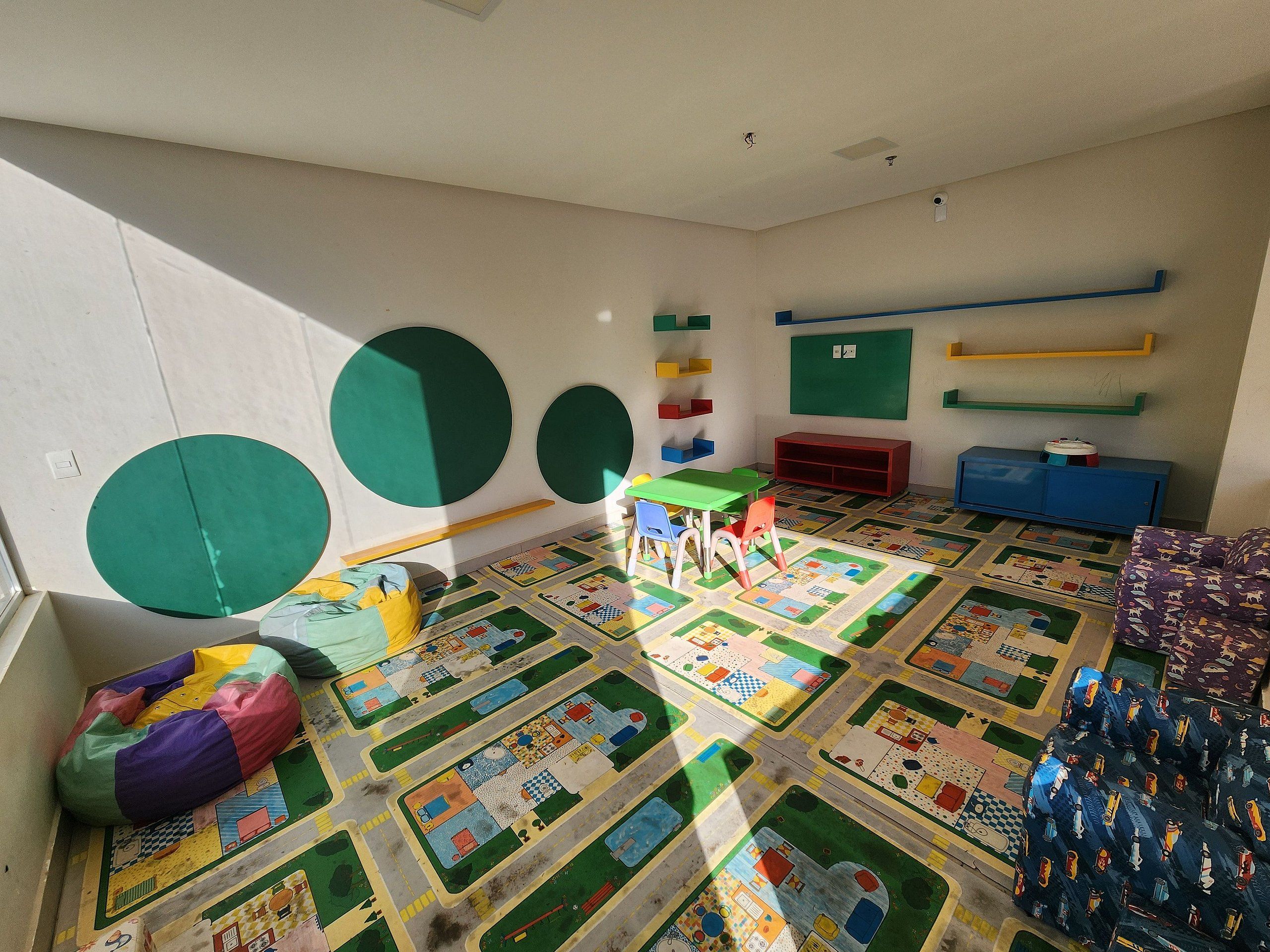 Una habitación con un tapete de juegos de colores, una mesa verde y un armario rojo.