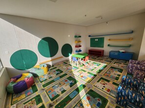 Ein Zimmer mit einer bunten Spielecke, einem grünen Tisch und einem roten Schrank.