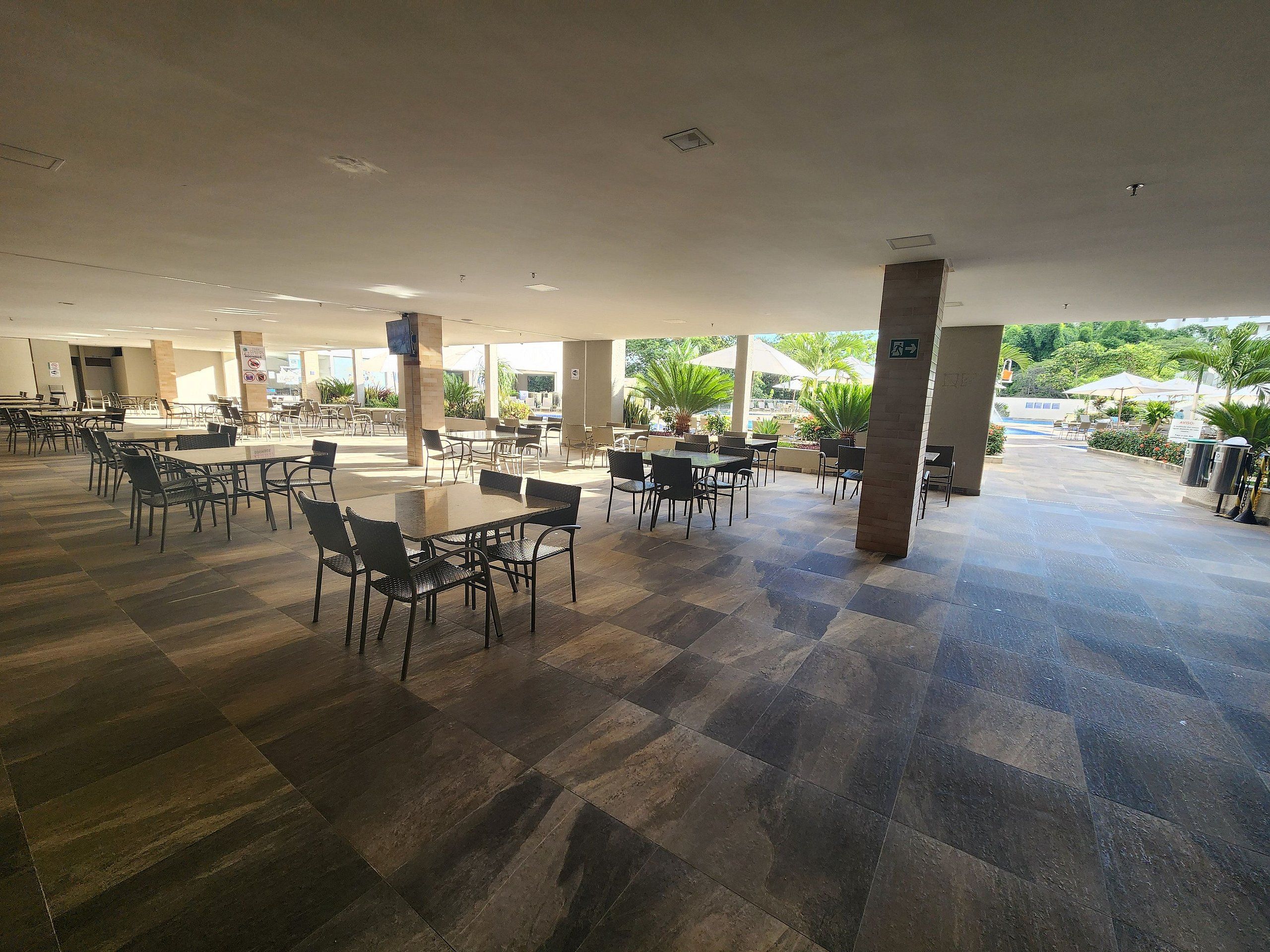 A spacious indoor area with multiple tables and chairs, a tiled floor, and a view of greenery outside.