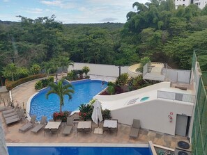 Ein Pool mit Liegestühlen und Tischen, umgeben von Grünpflanzen und einem Gebäude.