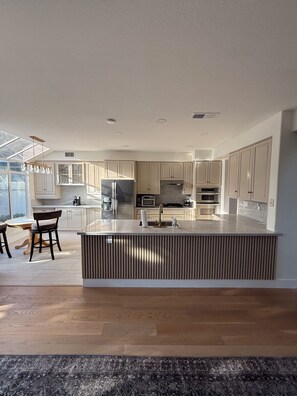 A modern kitchen with a central island, built-in appliances, and a dining area with chairs.
