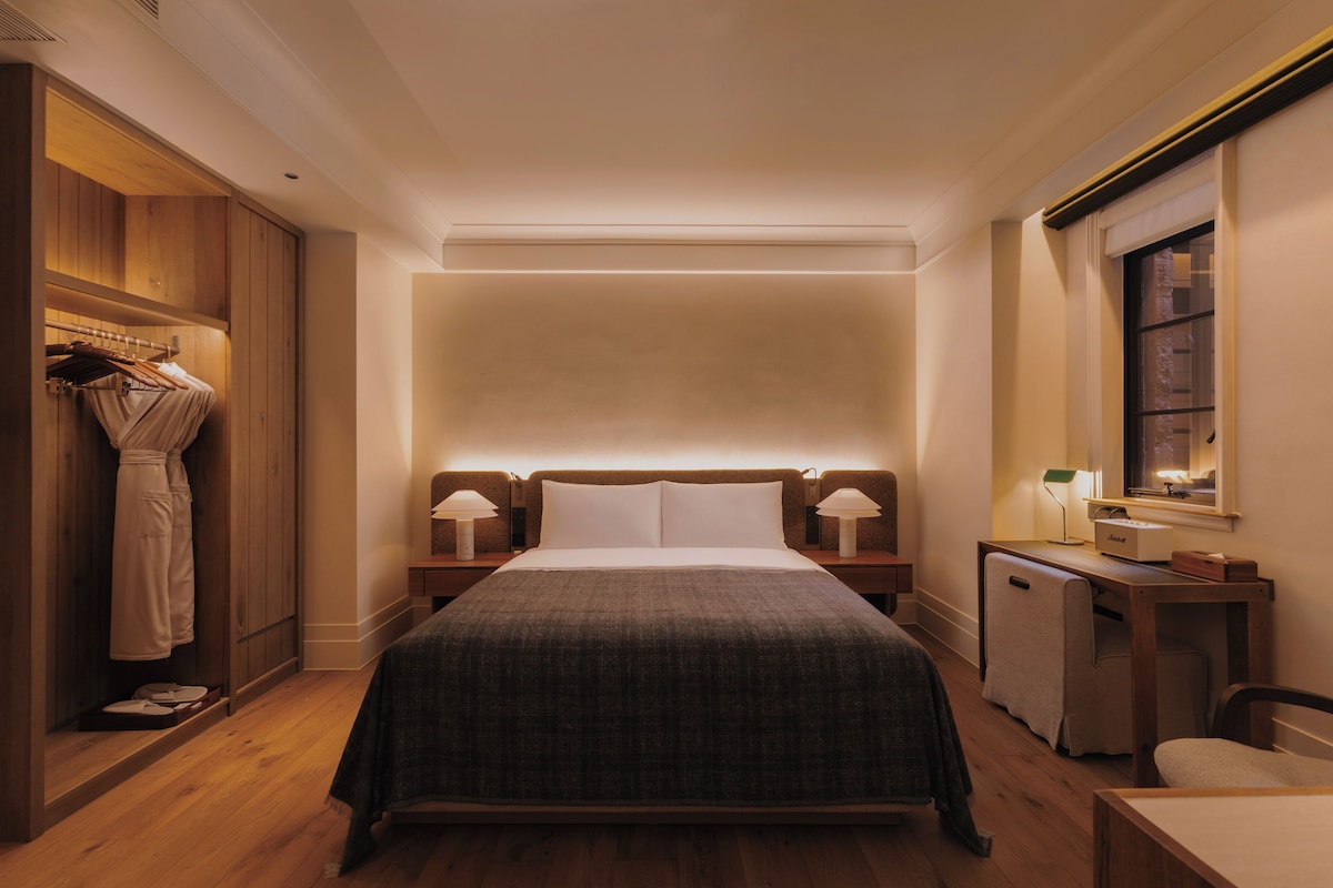 A hotel room with a large bed, bedside lamps, a wooden wardrobe, and a desk with a lamp.