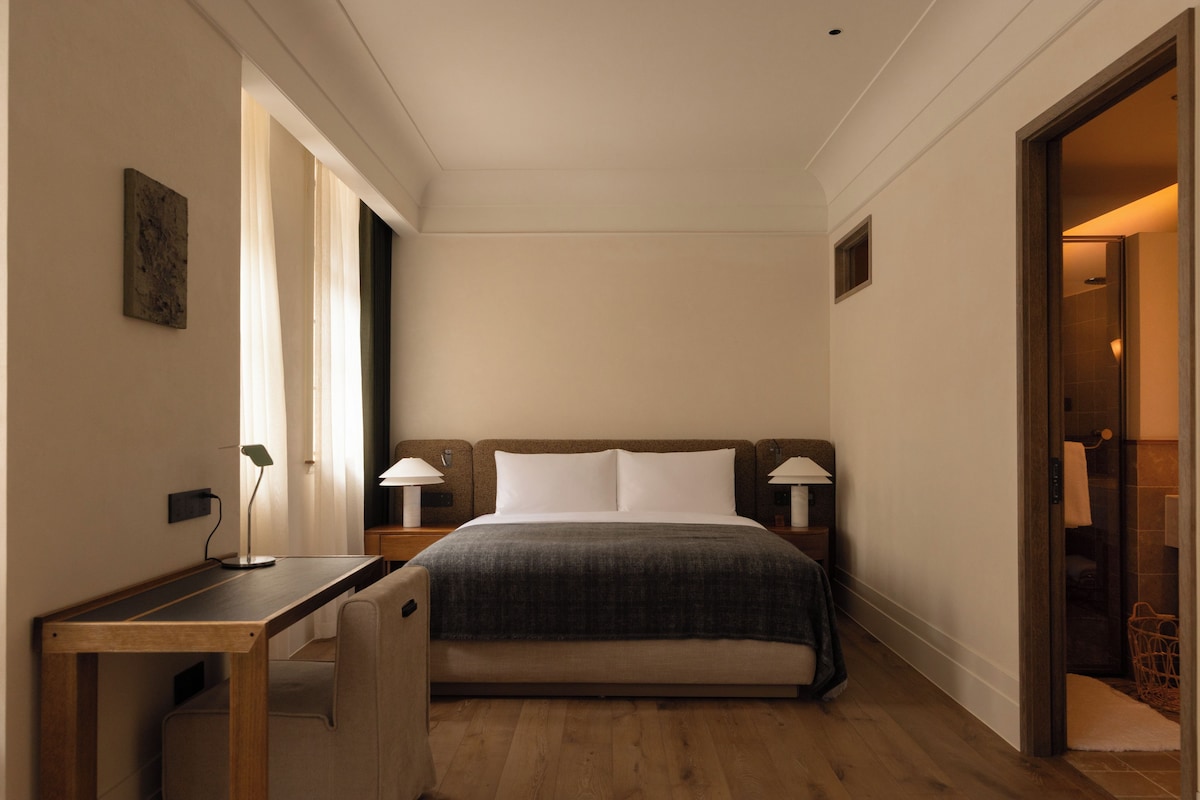 A hotel room with a bed, bedside tables, a desk, and a shower area.