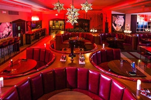 Ein Restaurant mit roten Ledersitzbänken, runden Tischen und einer zentralen Bar.