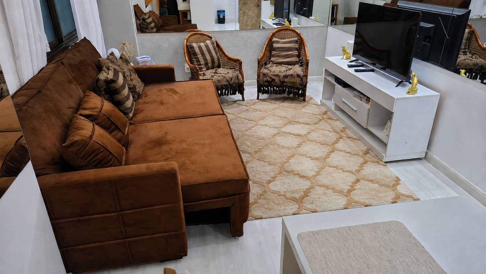 Un salon moderne avec un canapé marron, un tapis à motifs et un téléviseur posé sur un meuble blanc.