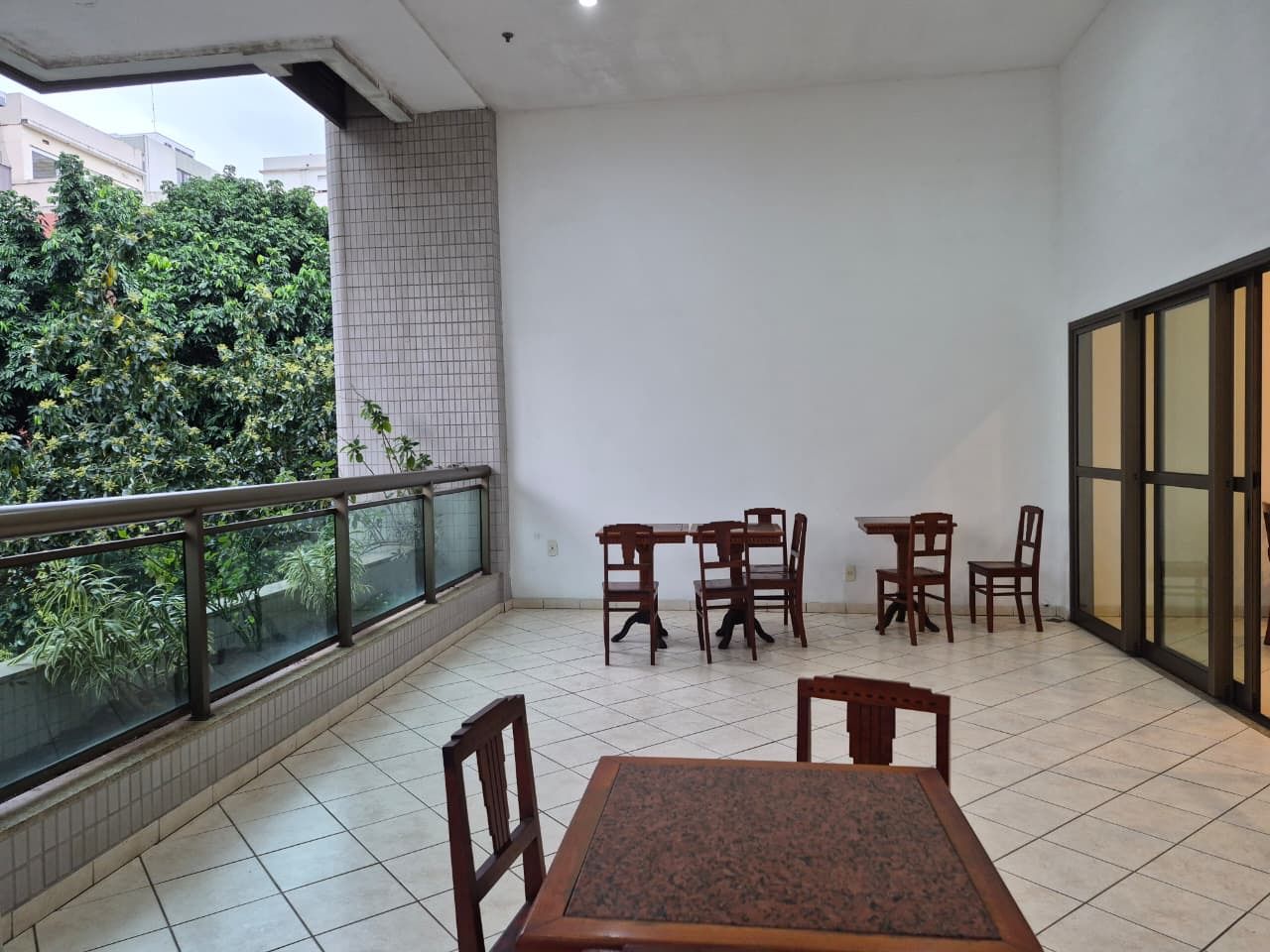 Ein Balkon mit Fliesenboden, einem Tisch und Stühlen sowie Blick auf Grünflächen.