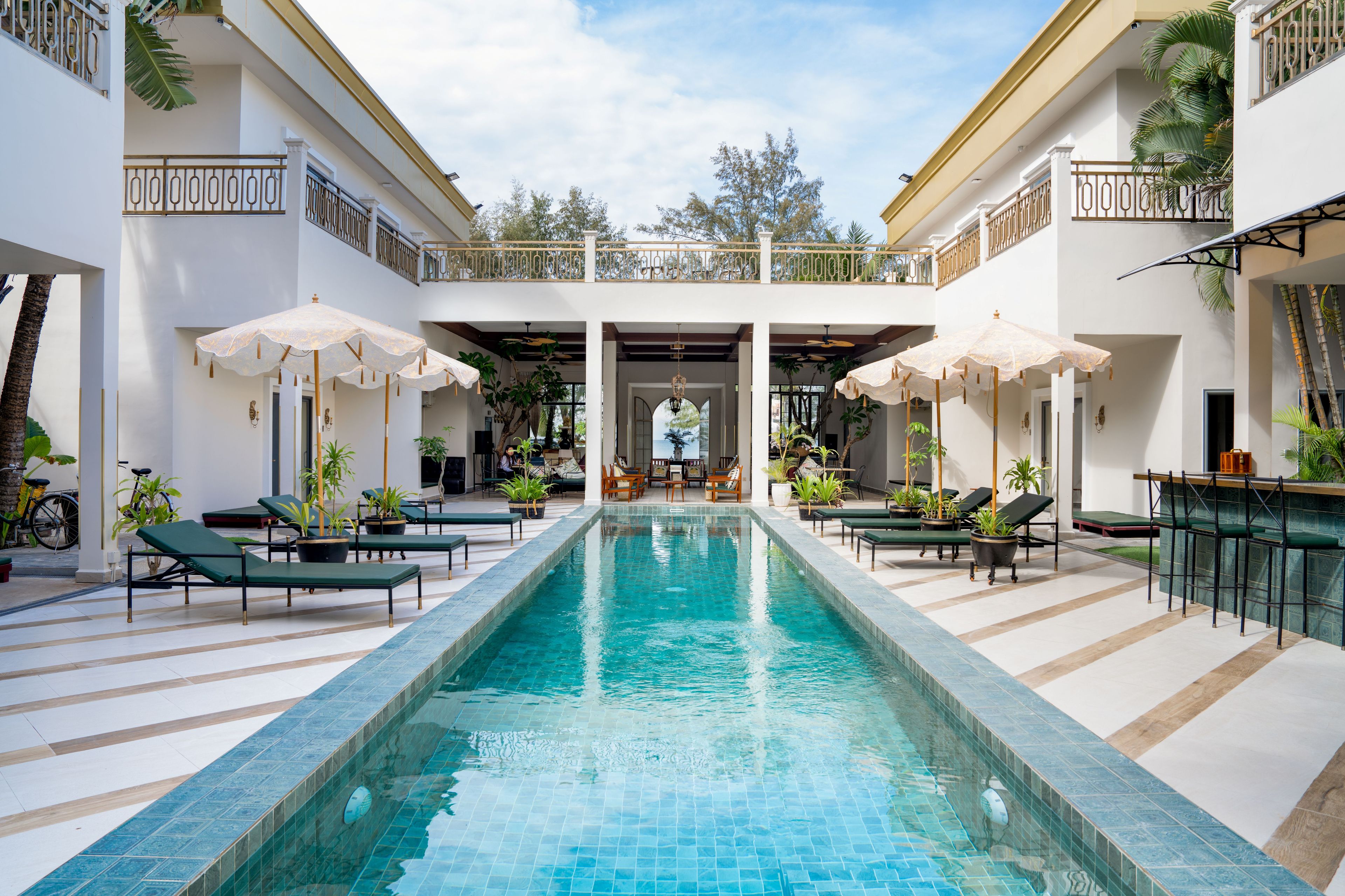 A swimming pool with lounge chairs and umbrellas, surrounded by white walls and potted plants.
