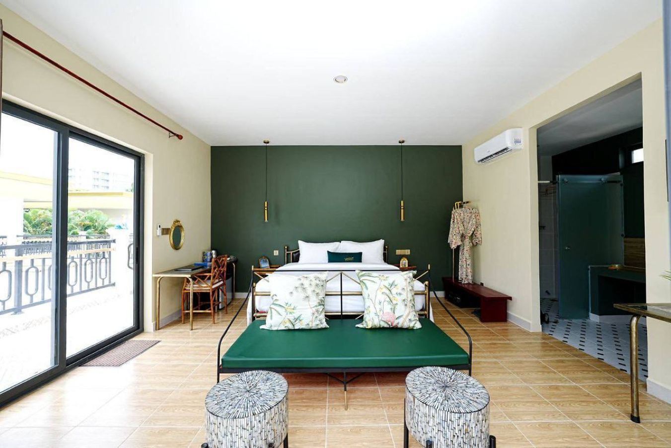A bedroom with a bed, a desk, and a chair, a balcony with a railing, and an air conditioning unit.