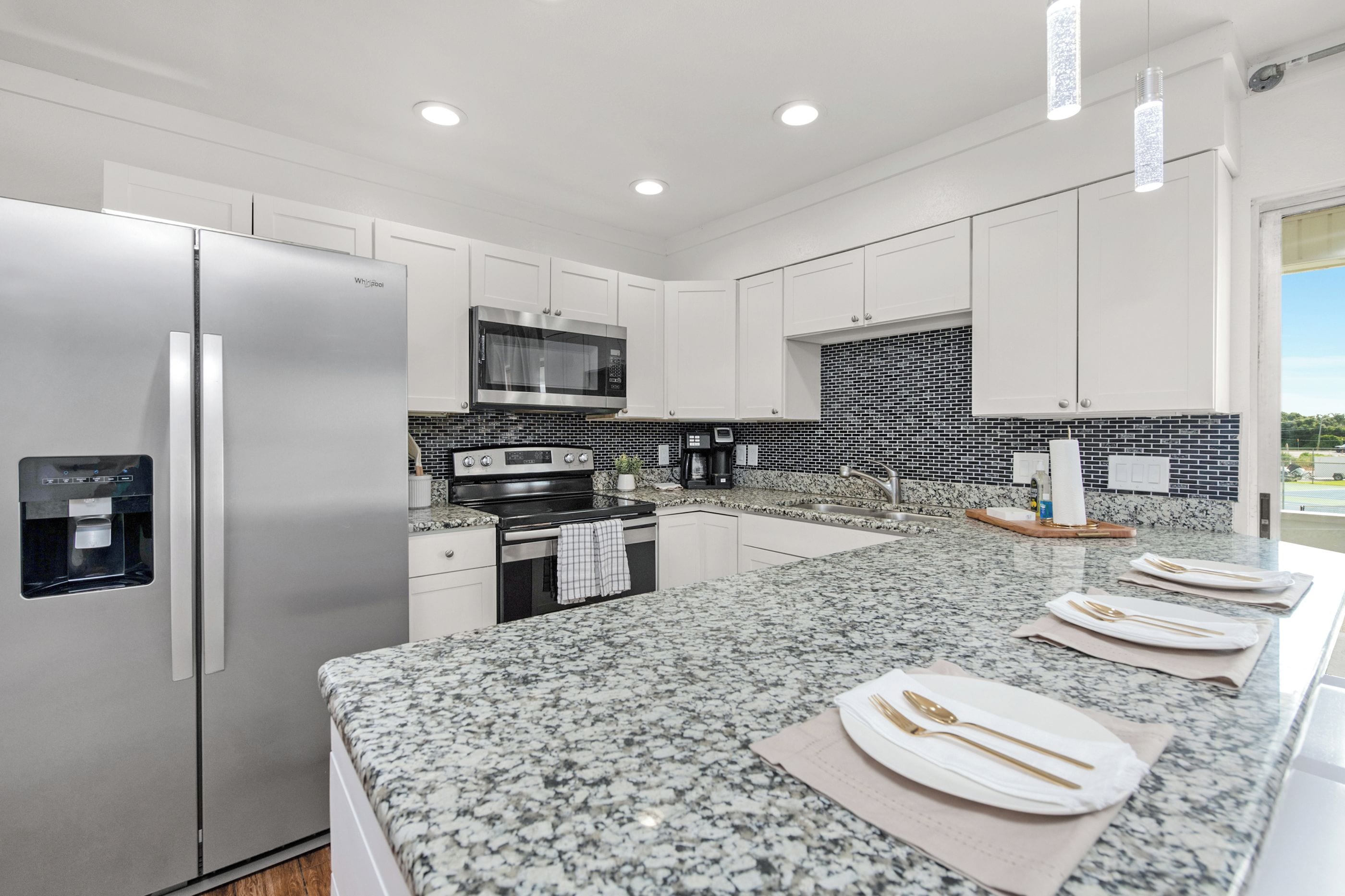 A modern kitchen with white cabinetry, a stainless steel refrigerator, a microwave, and a water dispenser.