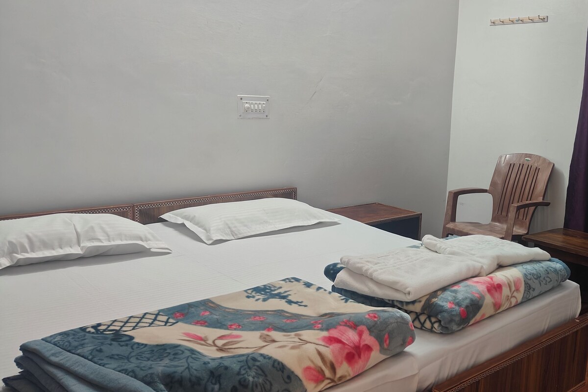 A single bed with a wooden headboard, a wooden nightstand, a desk with a chair, and a purple curtain.