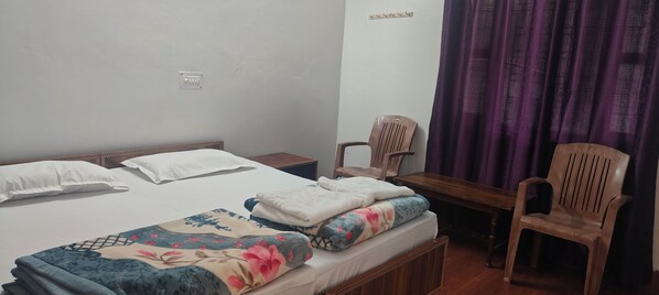 A single bed with a wooden headboard, a wooden nightstand, a desk with a chair, and a purple curtain. - Shantkunj (Uttarkashi)