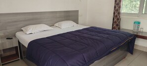 A neatly made bed with a dark blue quilt, a wooden headboard, and white pillows. - Shantkunj (Uttarkashi)