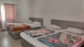 A hotel room with two beds, each with a wooden headboard, and a window with pink floral curtains. - Shantkunj (Uttarkashi)
