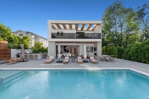 Ett modernt hus i två våningar med en swimmingpool, en uteplats och en välskött trädgård.