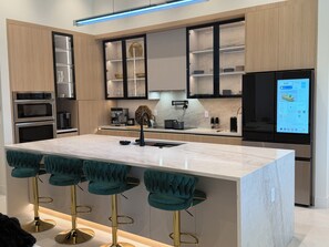 A modern kitchen with built-in appliances, a central island with bar stools, and a digital display. - Cape Sunset Paradise: Brand New Waterfront Luxury w/ Heated Saltwater Pool & Spa (Cape Coral)