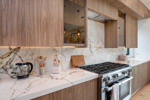 A modern kitchen with marble countertops, wooden cabinets, a gas stove, and a built-in oven. - Thayer Abode By Alora Reserve (Los Angeles)
