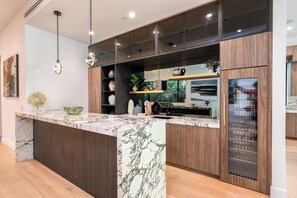 A modern kitchen with marble countertops, wooden cabinetry, and a built-in oven. - Thayer Abode By Alora Reserve (Los Angeles)