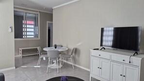 Uma sala de estar moderna com televisão de tela plana, mesa de jantar com cadeiras e um armário branco.