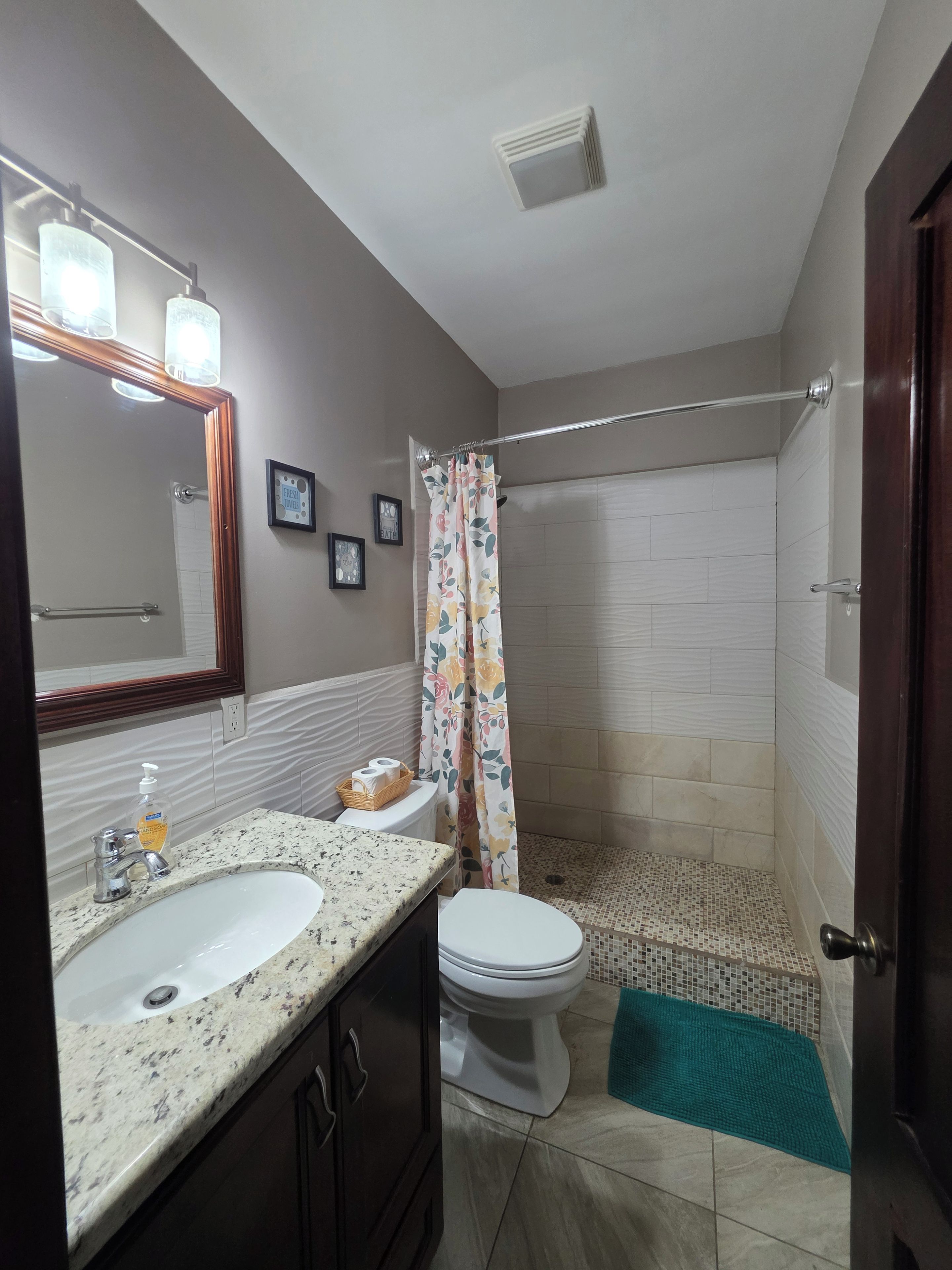 A bathroom with a sink, toilet, shower, and a mirror.