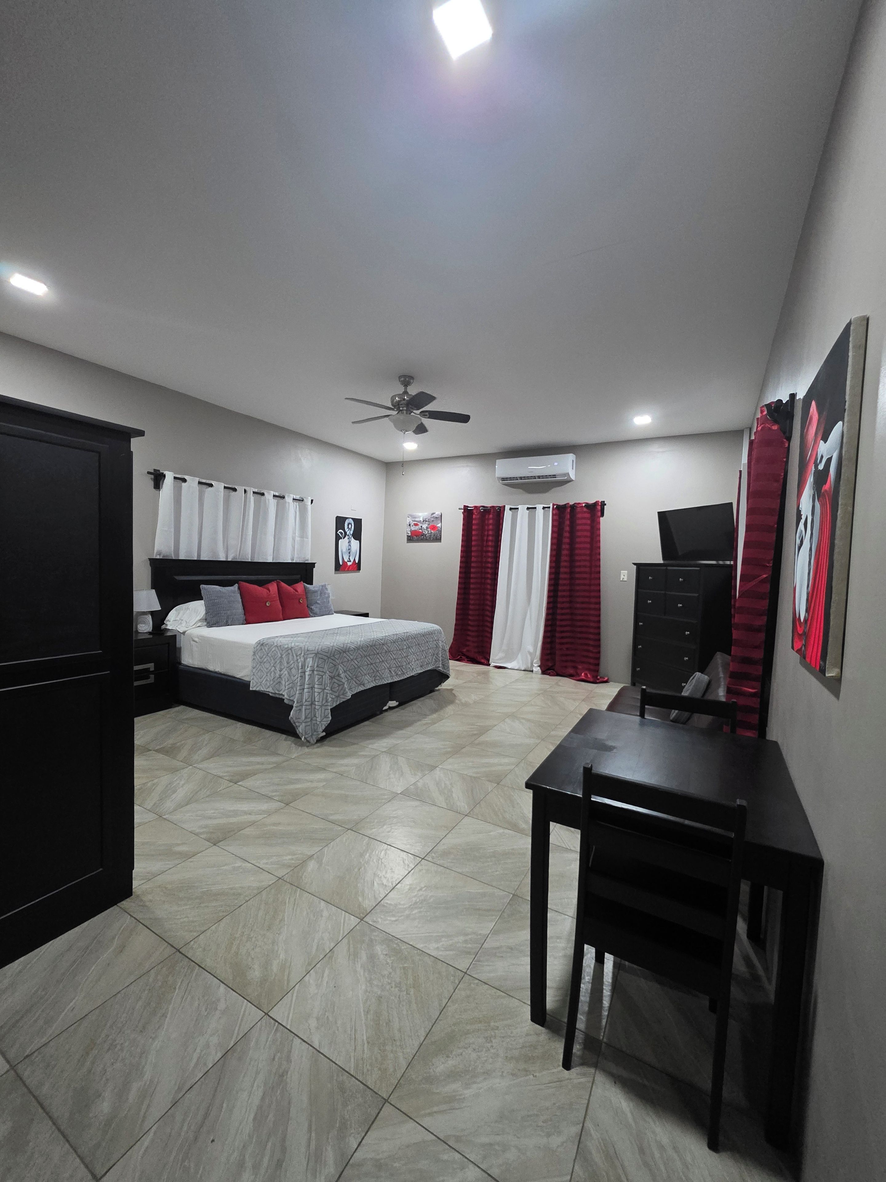 A bedroom with a bed, a desk, a wardrobe, and an air conditioning unit.