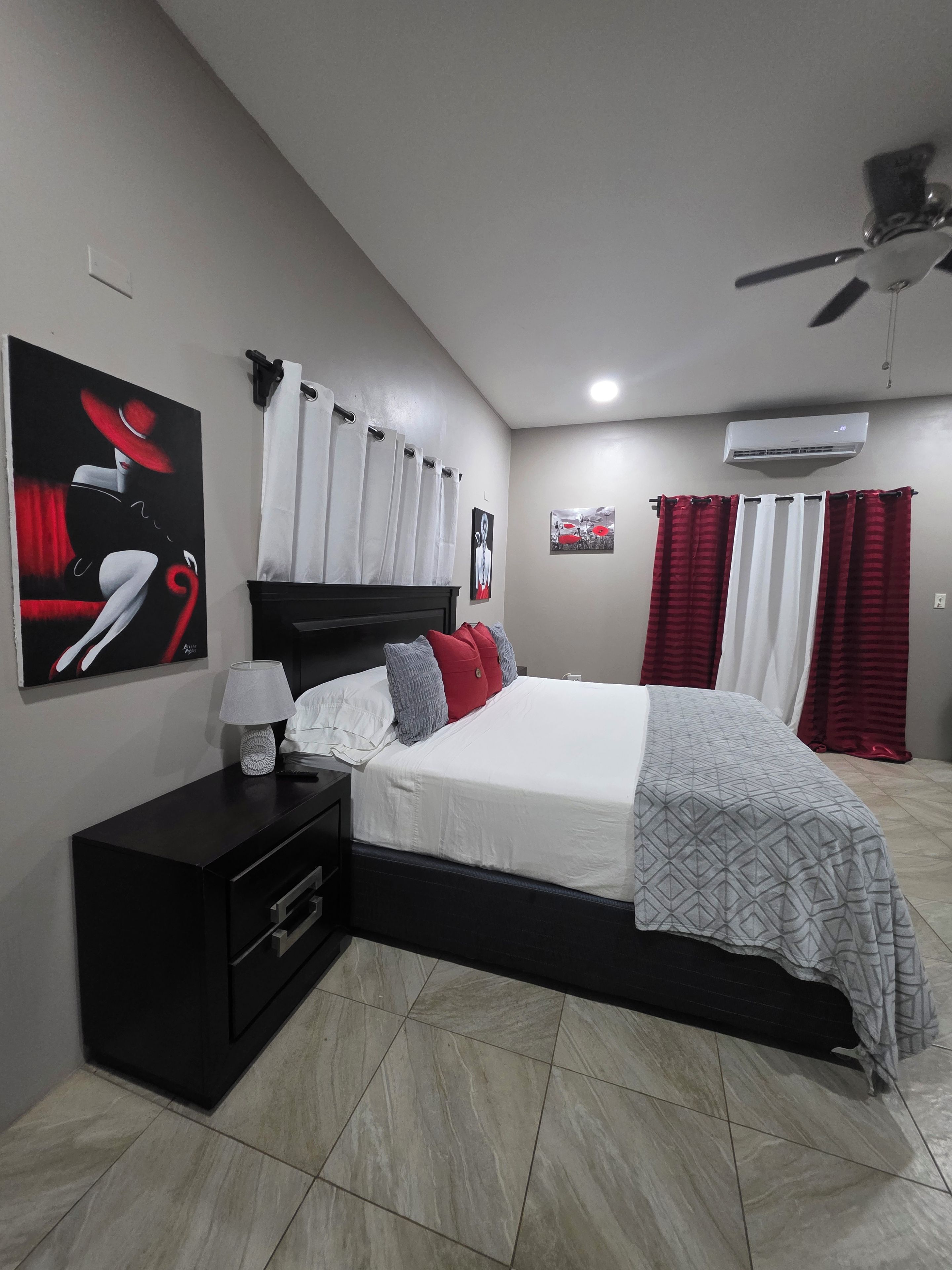 Un dormitorio con cama, mesita de noche, decoración en la pared, cortinas y aire acondicionado.