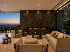 A modern living room with a fireplace, comfortable seating, and a city view. - Thrasher Aerie By Alora Reserve (Los Angeles)