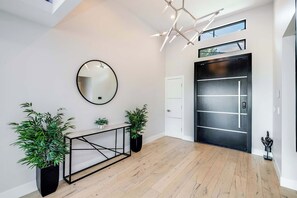 A modern interior with a wooden floor, a round mirror, a black-framed console table, and potted plants. - Wyndham Panorama By Alora Reserve (Los Angeles)