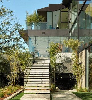 A modern building with a glass facade, a staircase leading to the entrance, and a well-maintained garden area. - Bel Air Peristyle By Alora Reserve (Los Angeles)