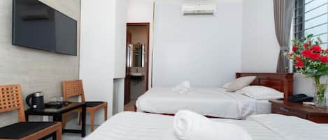 A hotel room with two beds, a TV, a coffee table, and a window with curtains.