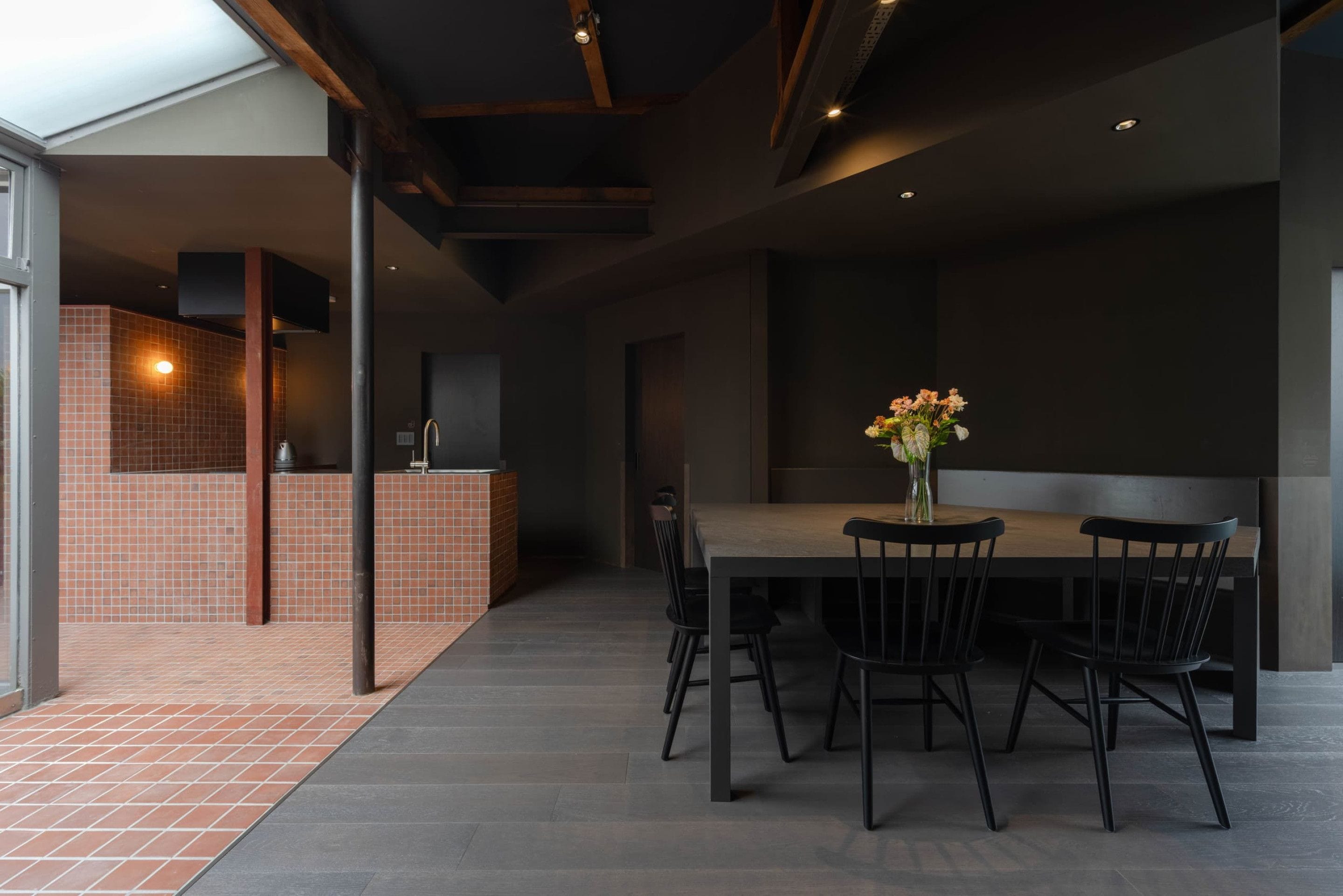 Un interior moderno con comedor que incluye una mesa y sillas, cocina con salpicadero de azulejos y un área exterior visible con suelo de baldosas.