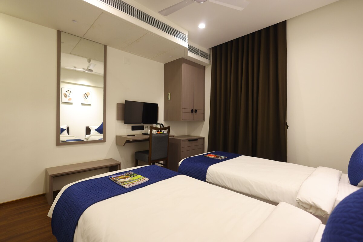 Hotellihuone, jossa on kaksi sänkyä, työpöytä, tuoli, televisio ja vaatekaappi.