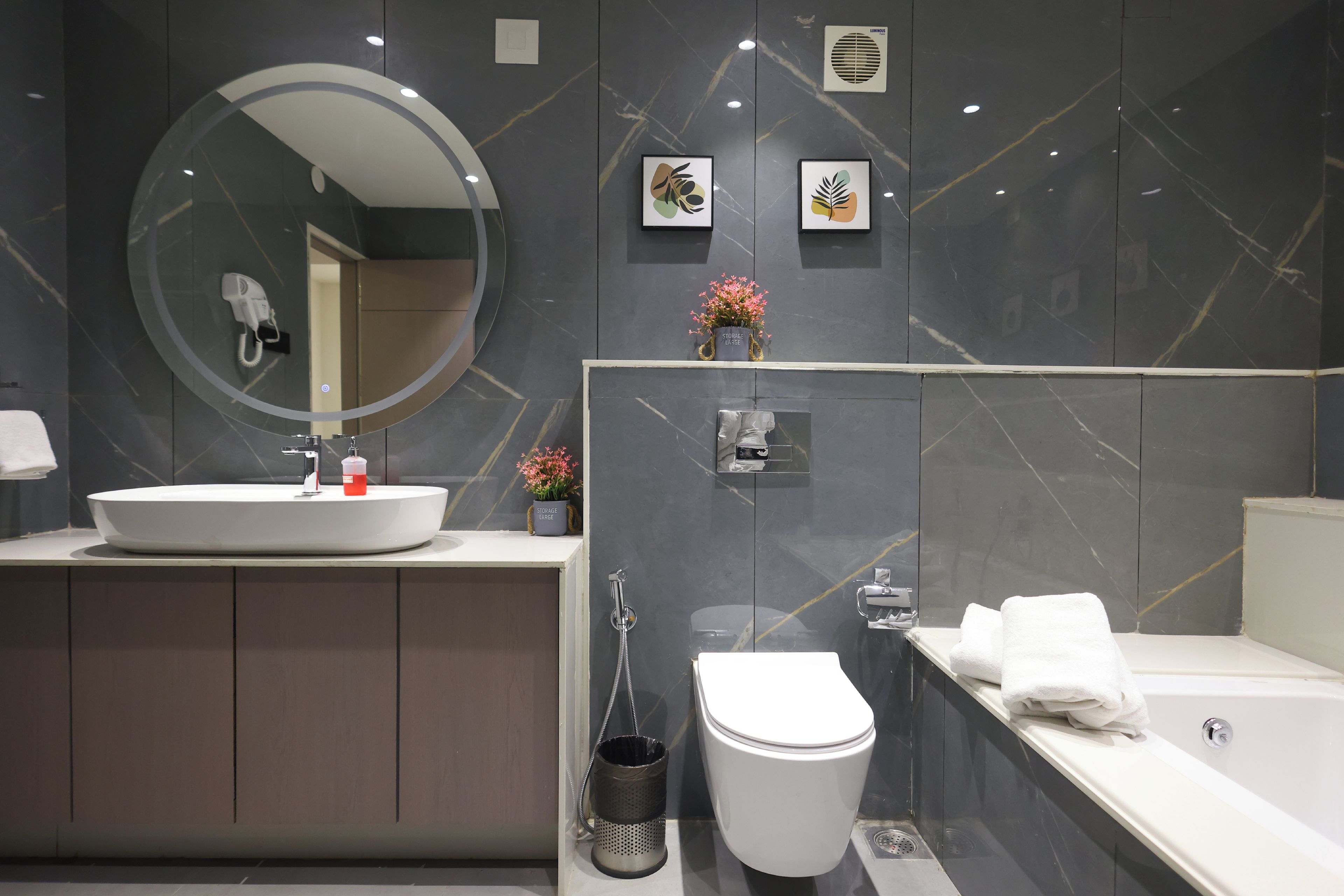 Een moderne badkamer met een ronde spiegel, een wastafel, toilet en bad.