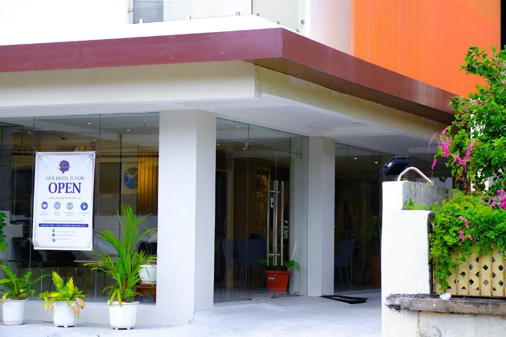A hotel entrance with a sign indicating it's open, glass doors, potted plants, and a modern building facade.